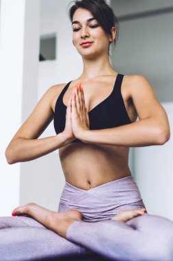 Uzun boylu, esmer, çıplak ayaklı, spor giyimli, Lotus pozisyonunda sabahları modern stüdyoda barış için yoga yapan bir genç.
