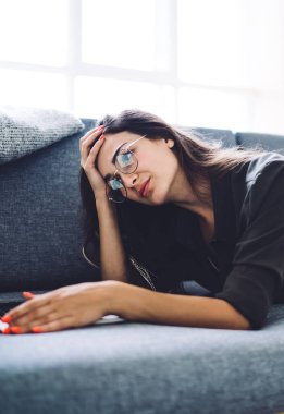 Rahat kanepeye uzanmış gözlüklü ve rahat bir şekilde dizüstü bilgisayar başında ev projesinde çalışırken odaklanmış genç bir kadının yan görüntüsü.