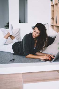 Ciddi bir beyaz kadın akıllı telefonuna bakıyor. Evdeki uzaktan kumandalı bilgisayardan rahatsız oluyor. Düşünceli yeniyetme kız evde boş zamanlarında sohbet etmek için dizüstü bilgisayar kullanıyor.