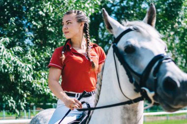 Doğa ortamını yeniden canlandırmak için hayvanlı hobiler, beyaz kadın profesyonel jokey güzel aygırla eyerleme hazırlanmak ve ata binmek için boş vakitlerin tadını çıkarıyor.