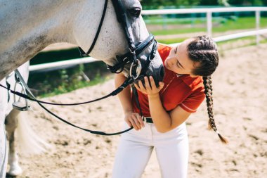 Güzel esmer profesyonel kadın jokey kırsal kesimde aygır atının yanında duruyor. Kadın binici, çiftlik çiftliğinde tatildeyken hayvan arkadaşına bakmaya ve onunla ilgilenmeye hazırlanıyor.