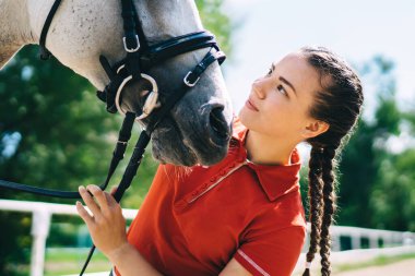 Beyaz giysili beyaz kadın sahibi, şirin beyaz atla boş zaman geçiriyor. Hafta sonunun tadını çıkarıyor. Favori hobisi, çiftlik çiftliğinde hayvanlarla ilgilenen genç kadın jokey.
