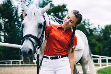 Çiftlik otlaklarında at binme hobisi sırasında günlük kıyafetlerini giymiş beyaz bir kadın at, safkan şampiyon aygırla ilgilenir.