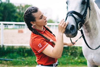 Beyaz tenli profesyonel at binicisi, doğa ortamında duran ve at ile konuşan arkadaş hayvanlarla ilgilenir. Genç esmer kız, at sporu için gün harcar.