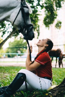 Beyaz kadın jokey sevimli aygır atına iyi bak. Koşum eğitimi için dost canlısı bir hayvanla hafta sonunun tadını çıkar. 20 'li yaşlarda genç bir kadın safkan kısrakla iletişim kuruyor.