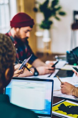 Çeşitli yaratıcı erkek ve kadın tasarımcılar birbirleriyle iletişim halindeler ve ofiste toplantı masasında dizüstü bilgisayarla birlikte otururken kooperatif süreç hakkında konuşuyorlar.