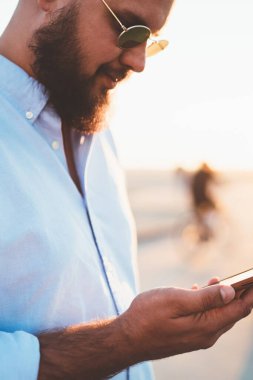 Erkek hipster haber online holding smartphone posta denetimi metin mesajı ve şehir üzerinde cep telefonu app duran üzerinde sokak günbatımında gönderme sokak, şık yakışıklı delikanlı okuma görünümünü kırpılmış