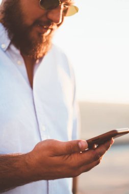 Bir smartphone cep telefonu ile posta açık havada kontrol gelir mesaj okuma, sosyal ağlar üzerinde iyi bir bağlantı üzerinden telefon app--dan online video izlerken hipster adam sakallı rahat gömlek giymiş adam yakın çekim