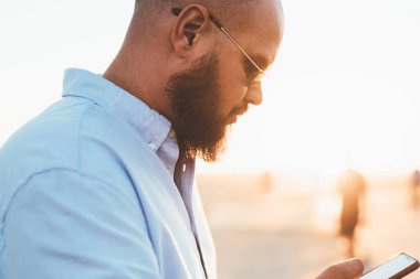 Genç erkek holding smartphone sokak, yakışıklı hipster adam serbest zaman sırasında cep telefonu kullanarak sosyal ağlarda online video izlerken vakit kafe hakkında bilgi tarama sakallı