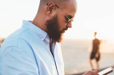 Dalgın sakallı adam akıllı telefon hücresel açık havada duran üzerinden sosyal ağlar bloglama içerik yükleme sokak, erkek hipster üzerinde iyi bir internet bağlantısı üzerinden uygulama yükleme