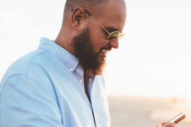 Hipster adam akıllı telefon app ağlardan online video izlerken güneş gözlüğü bağlantısı ile yakışıklı genç adam haber Gözat web sayfasında modern telefon güneşli hafta sonu dinlenme okuma memnun.