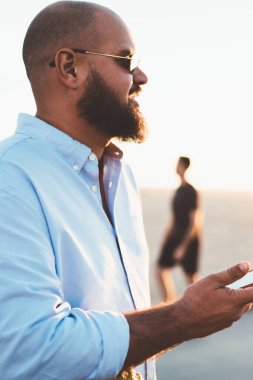 Sakallı adam cep telefonu online sosyal ağlar tatilden gezici pay fotoğraf 4 g bağlantısında hipster adam memnun yaz akşamında, tadını çıkarırken sohbet üzerinden kısa mesaj gönderme