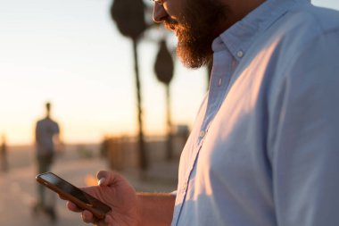 Genç adam erkek hipster smartphone holding modern uygulama Tebliği kontrol sokak, kırpılmış görünümü üzerinde duran cep telefonu 4 g bağlantısı kullanma sosyal ağlardan video izliyor sakallı