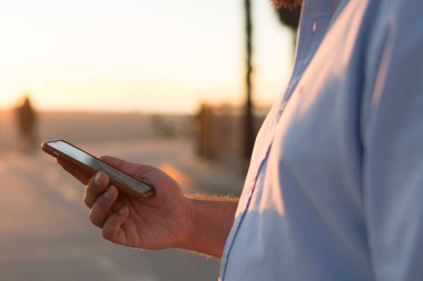 Genç adam online şehir sokak, hipster adam pay fotoğraf blog yolu ile uygulama açık havada süre sosyal ağlar posta kontrol üzerinde ayakta rezervasyon yapmak için smartphone kullanarak görünümünü kırpılmış