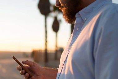 Hipster adam modern cep telefonu elinde göz web sayfasından, genç adam 4 g internet bağlantısı açık havada duran kullanarak Smartphone'da kısa mesaj gönderme haber okuma görünümünü kırpılmış