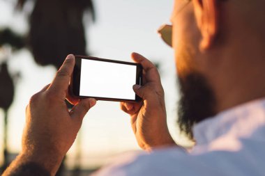 Erkek blogger fotoğraf çekmek için sahte ekranı ile smartphone kullanarak görünümünü sırt ve ağlarda, modern cep telefonu fotoğrafları yaz tatillerini akşamları sırasında yapma hipster adam pay