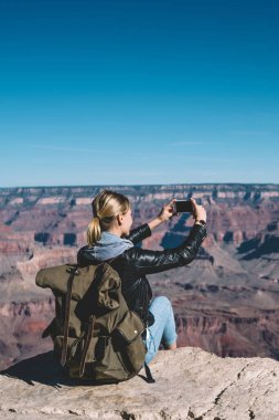 Genç hippi kız Yolculuk tutkusu ile resim üzerinde kayalık uçurum ABD, kadın turist sahne görünümü telefon aracılığıyla Büyük Kanyon peyzaj fotoğrafçılık seyahat yapmak için smartphone kamera ile sırt çantası