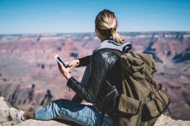 Arkadan görünüş kadın seyahat telefon veri ağ sohbet için vahşi çevre holding smartphone içinde hippi kız Yolculuk tutkusu memnun yüksek dağ tepe üzerinde oturan bağlantıda kontrol
