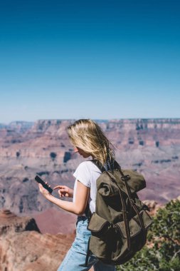 Genç hippi kız posta etkin hafta sonu, kadın turist tur sırasında iletişim kurmak için vahşi doğada iyi mobil veri bağlantısı kullanarak sırt çantası ile dağlarda hiking smartphone cep telefonu ile kontrol