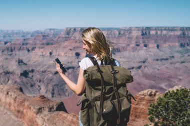 Genç hippi kız okuma mesajı smartphone ayakta dağlar bakış açısı gezici, kadın turist tur sırasında iletişim kurmak için doğada iyi mobil veri bağlantısı kullanarak sırt çantası ile kullanma