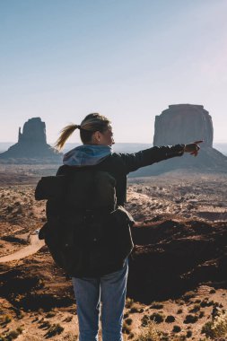 Arkadan Görünüm Monument Valley güzel manzara kumtaşı oluşumu ile işaret eden sırt çantası ile genç kadın Gezgin, hippi Kız Navajo rezervasyonu hiking sırt çantası ile keşfetmek benzersiz Jeoloji