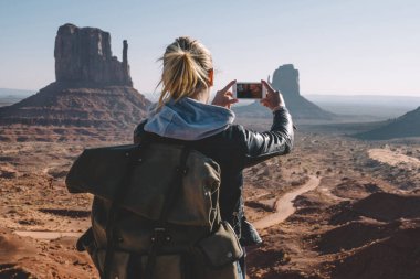 Monument Valley smartphone kamera, resim yapma ABD doğasını keşfetmek kumtaşı oluşumu telefonla hippi kız ile manzara manzara fotoğrafçılığı sırt çantası ile arkadan görünüşü erkek