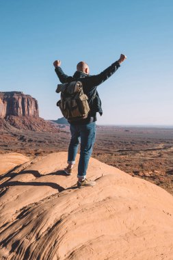 Arkadan görünüşü erkek traveler ABD ayakta yüksek tepede, sırt çantası duygu özgürlük Monument Valley oluşumunda scenerysandstone bakarak kaya üzerine adamla hipster başarılı yolculuk kutluyor