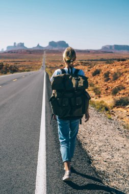 Hippi kız Yolculuk tutkusu güneybatı Milli Parkı yürüyerek, kadın turist için yolda otostop Arizona yolculukta sahip sırt çantası ile alma konusunda vahşi topraklarda asfalt yolda yürürken arkadan görünüm