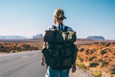 Arkadan Görünüm kadın Gezgin vahşi geçen asfalt yol keşfetmek güneybatı ABD hippi kız otostop ile yolculuk sahip karayolu üzerinde yürüyen sırt çantası ile aktif yaşam tarzı zevk toprakları.