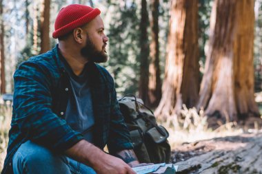 Uzağa yolculuk ulusal park harita ormandaki ile oturma sırasında vahşi çevre keşfetmek erkek yolcu Yolculuk tutkusu açık havada, kalan süre ahşap manzara bakarak sırt çantası ile genç hipster adam uzun yürüyüşe çıkan kimse