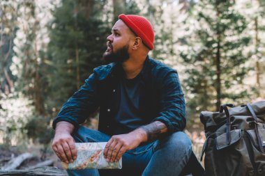 Sakallı erkek yolcu uzağa ahşap vahşi doğa tur, trekking, ahşap peyzaj çevre zevk ormandaki sırt çantası ile oturan hipster adam hiking sırasında keşfetmek eski ağaç üzerinde arıyor