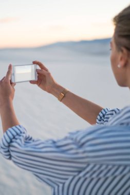 Arkadan görünüşü güzel doğa günbatımı görünüm ABD'de yaz tatil gezisi sırasında fotoğraf çekmek telefonu kamera kullanan hippi kız White Sands tepeleri, resim yapma kadın holding smartphone