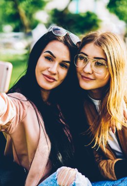 Smartphone uygulama kullanarak akıllı güzel resim yapma neşeli arkadaşlar. Çekici genç kadın üzerinde modern telefon açık havada hafta sonu serbest zaman sırasında poz selfie yapma