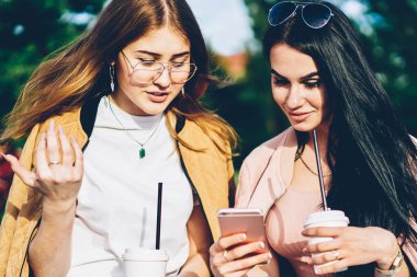 Esmer blogger posta lezzetli kahve zevk bankta oturan modern telefon aygıtı üzerinde en iyi arkadaşı için Internet Web sitesinde gösterilen. Hippi kız giyim fotoğraflarını smartphone açık havada üzerinde tartışıyor