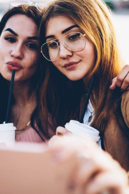 Görüntü lezzetli kahve ön kamera dijital hareket eden telefon aygıt üzerinde seyir ve kentsel ortamda dostu toplantı sırasında fotoğraf çekmek elinde olan çekici gülümseyen genç kadın kapatmak