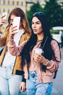 Elinde yeni şehirde yürüyüş ve modern telefon cihazları üzerinde fotoğraf yapma kahve ile iki kadın turist. En iyi arkadaşlar gezginler smartphone üzerinde serin fotoğraf çekmeye kentin güzelliği hayran