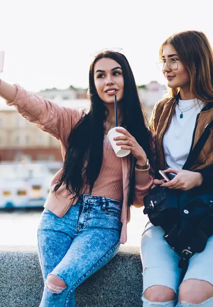 İki güzel gezginler yapma selfies fotoğraflar üzerinde modern telefon ayakta zekâ kahve ve sırt çantası şehir promosyon arka plan üzerinde reklam için reklam alanı yakınında şık casual kıyafet ile
