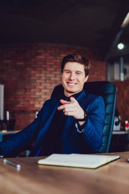 Masaüstünde oturan başarılı erkek yönetmenin portresi kameraya bakıyor ve neşeli ruh halinin keyfini çıkarıyor, resmi olarak pozitif iş adamı şirket ofisinde heyecanlı ve mutlu hissederek zaman geçiriyor.