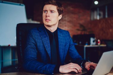 Takım elbiseli, kafası karışık bir iş adamı bilgisayarında bilgisayarlı bir cihazla yeni başlatılan proje üzerinde kafa yoruyor. Düşünceli erkek iş arkadaşı, modern netbook aracılığıyla iş arkadaşlarıyla iletişim kuruyor.