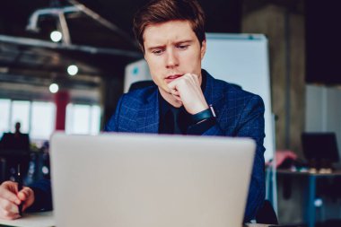 Şaşkın erkek çalışan önemli web sitelerini izlerken ders kitabında ana bilgileri yazarken, düşünceli beyaz girişimci sosyal ağlarda haberleri okurken modern netbook 'ta 4G bağlantısı kullanıyor.