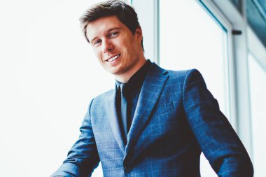 Pencerenin yanında durup kameraya bakan başarılı beyaz erkek portresi, şirket ofisinde boş zamanlarında poz veren pozitif gülümseyen iş adamı, liderlik ve istihdam kavramı