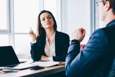 Kendine güvenen erkek yönetmen, genç internet reklamları, iş ve takım çalışması kavramları için ekran oluşturarak dizüstü bilgisayarın önünde oturan meslektaşlarına çalışma sürecini anlatıyor.