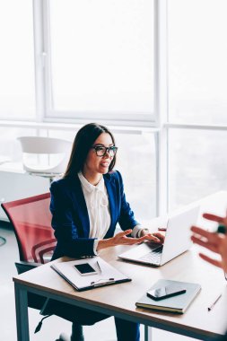 Genç beyaz iş kadınının dizüstü bilgisayarla masada oturması ve iş arkadaşlarıyla şirket sorunlarını çözmesi, genç bayan girişimcinin konferans sırasında ortaklarıyla konuşması