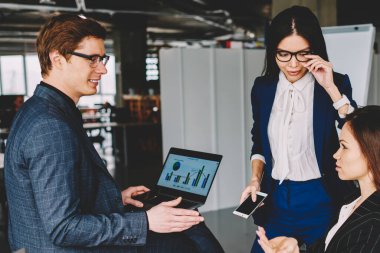 Bir grup erkek ve kadın girişimci ofiste birlikte vakit geçirirken fikirleri tartışıyor, iş adamı dizüstü bilgisayarla masada oturuyor ve iş arkadaşlarıyla verimlilik grafiği hakkında konuşuyor