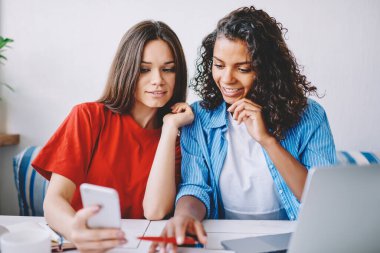 Başarılı hipster kızları cep telefonlarıyla komik komedi programı izliyorlar ücretsiz üniversite internetine bağlanıyorlar, mutlu pozitif kız öğrenciler sosyal ağlarda haberleri modern telefon aygıtıyla okuyorlar.