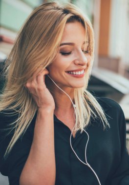 Elektronik kulaklıklı mutlu bir kadın çevrimiçi video yayınları izliyor ve gülümsüyor, modern kulaklıklı neşeli bir kadın dijital tablet tutuyor ve müzik podcast 'i dinlerken haber okuyor.