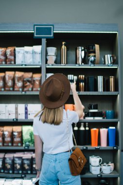 Kafkasyalı yeniyetme kızın modaya uygun kıyafetler giyip kafeteryadaki rafların yanında termodinamik bardakları seçen 20 'li yaşlarda genç bir kadının kafeteryadaki modern kavanozlara ve içeceklere baktığı görüntüler.