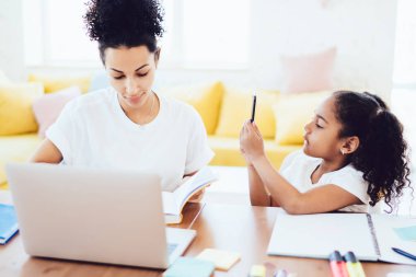 Afrika kökenli Amerikalı bir anne okul not defterinde telefon kullanan ve annesinin ödevlerini yaparken dikkatini dağıttığını hayal eden küçük bir kızla notları kontrol ediyor.