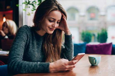 Gülümseyen başarılı bayan öğrenci, modern cep telefonuyla internet sitesinde komik video blogu izlerken rahat kafeteryada dinlenirken, milenyum yaşam tarzı konsepti ve gelişmiş teknoloji