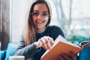 Neşeli kız öğrenci portresi. Kapalı bir yerde oturmuş ve gelecek için planlar yapıyor. Mutlu, zeki hippi kız boş zamanlarını birlikte çalışarak geçiriyor ve kameraya bakıyor.